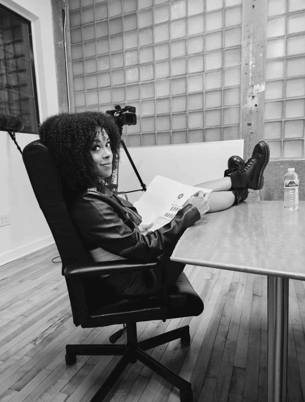 Aliyah Celeste seated with a script, looking toward the camera in a black-and-white behind-the-scenes portrait.