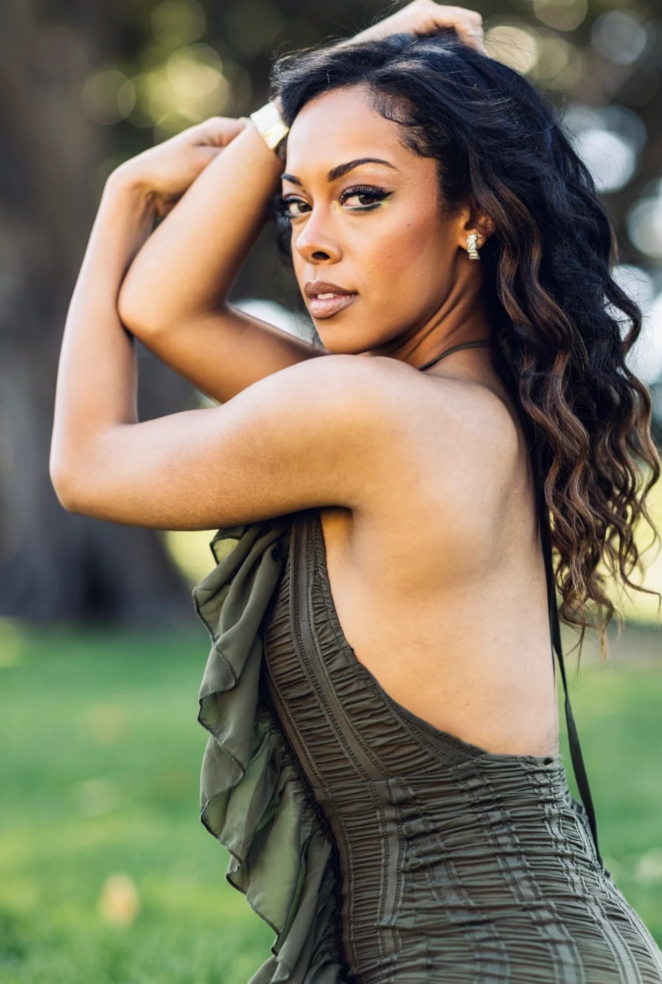 Aliyah Celeste looking over her shoulder outdoors in an olive dress.